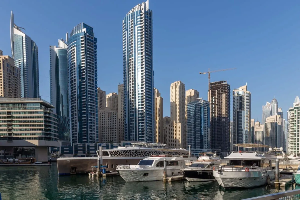 A marina with boats sits in front of a waterfront skyline of tall buildings.