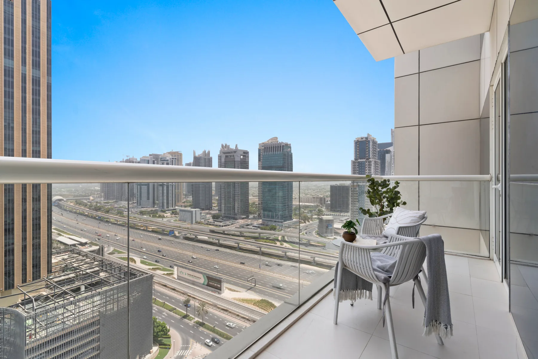 A balcony seating area overlooks a multilane road and nearby high-rise buildings.