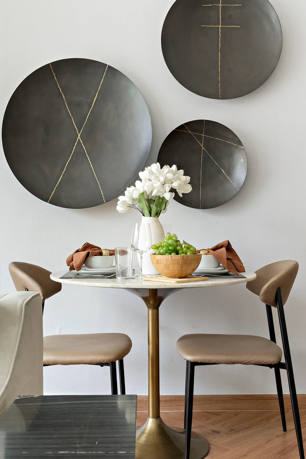 A dining area with a round table, upholstered seating, and dark circular wall decor.