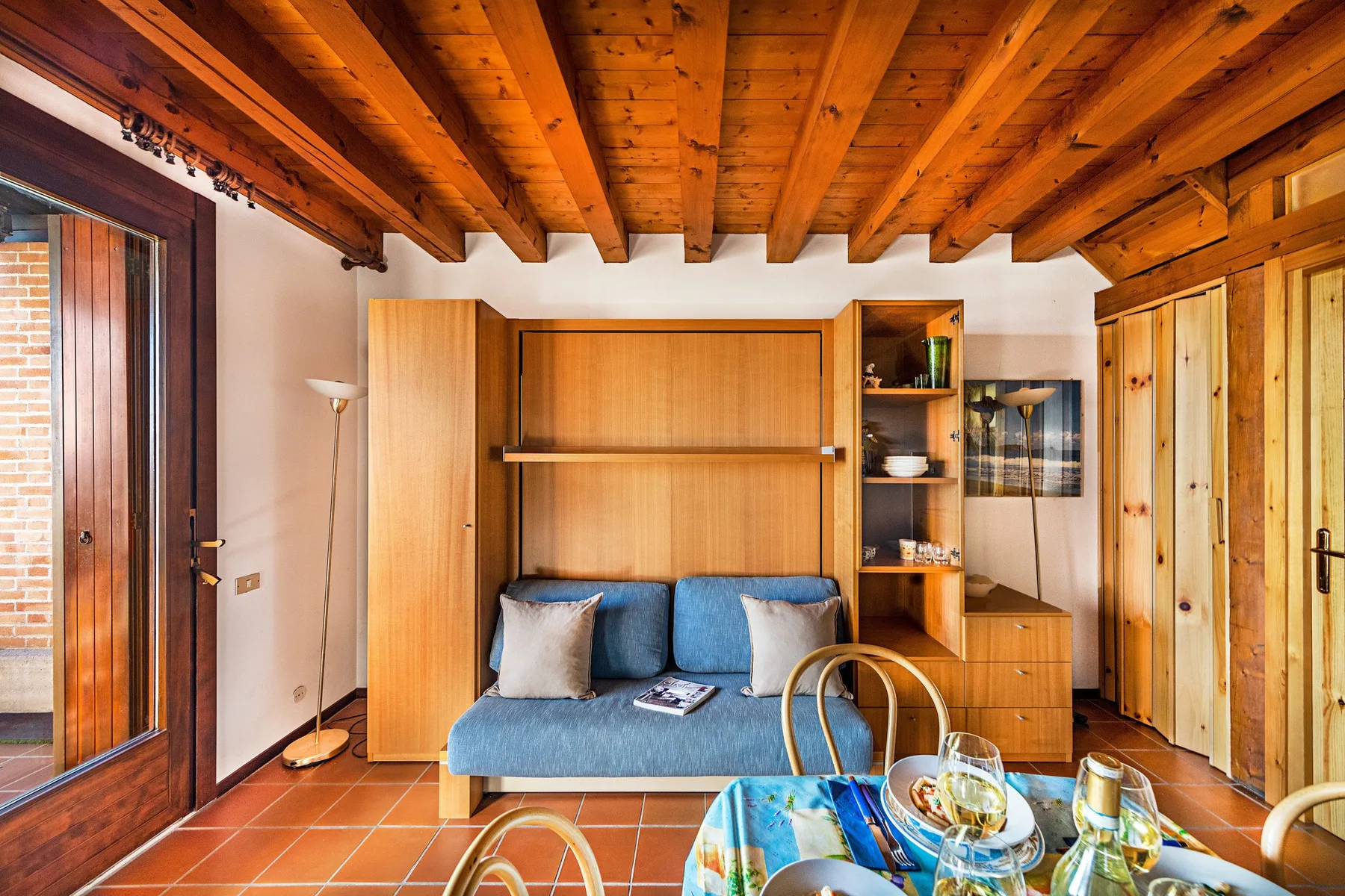 A warm living area with a blue sofa beneath exposed wooden ceiling beams.