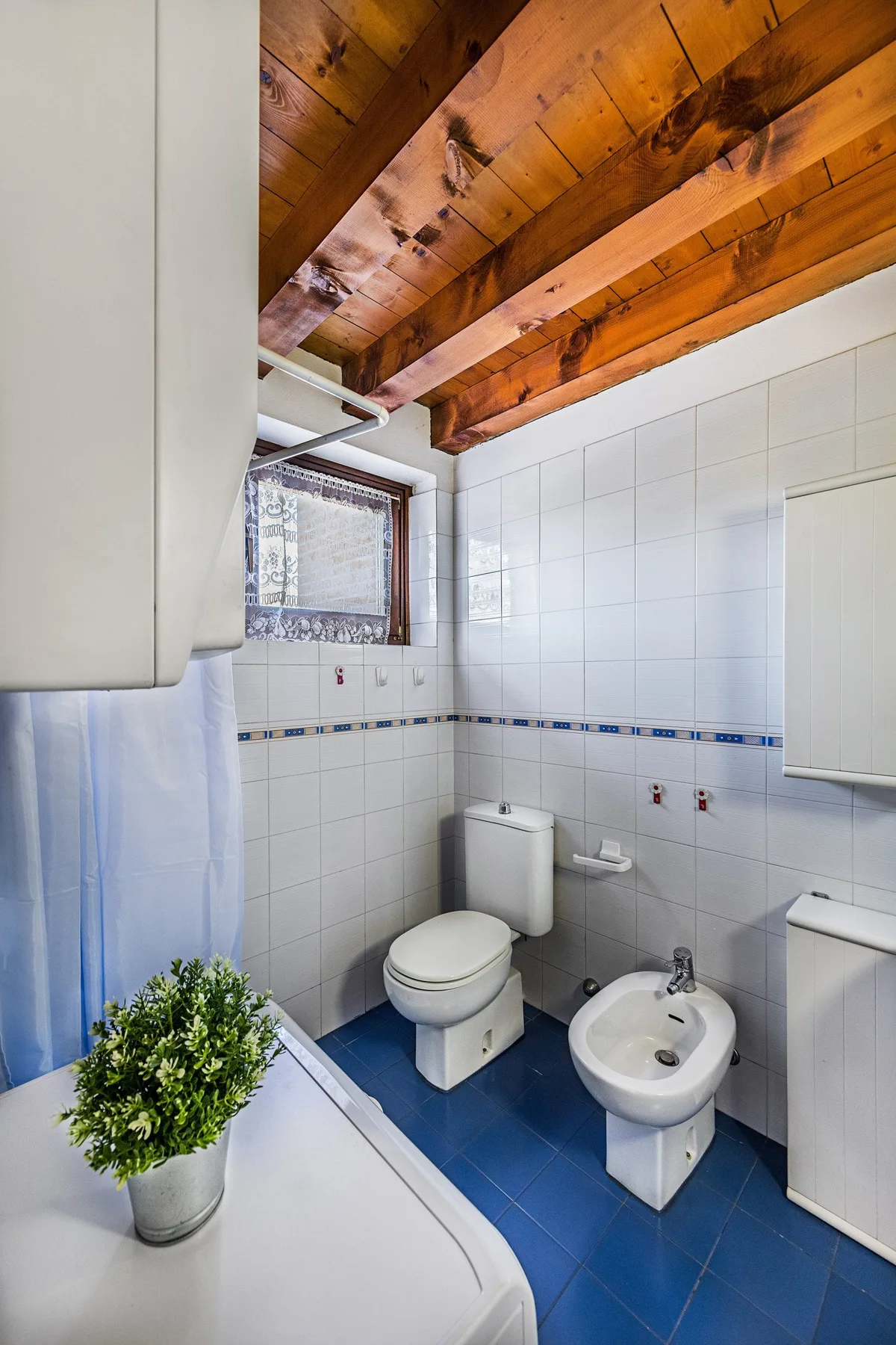A tiled bathroom with a bathtub, toilet, and bidet beneath exposed wooden ceiling beams.