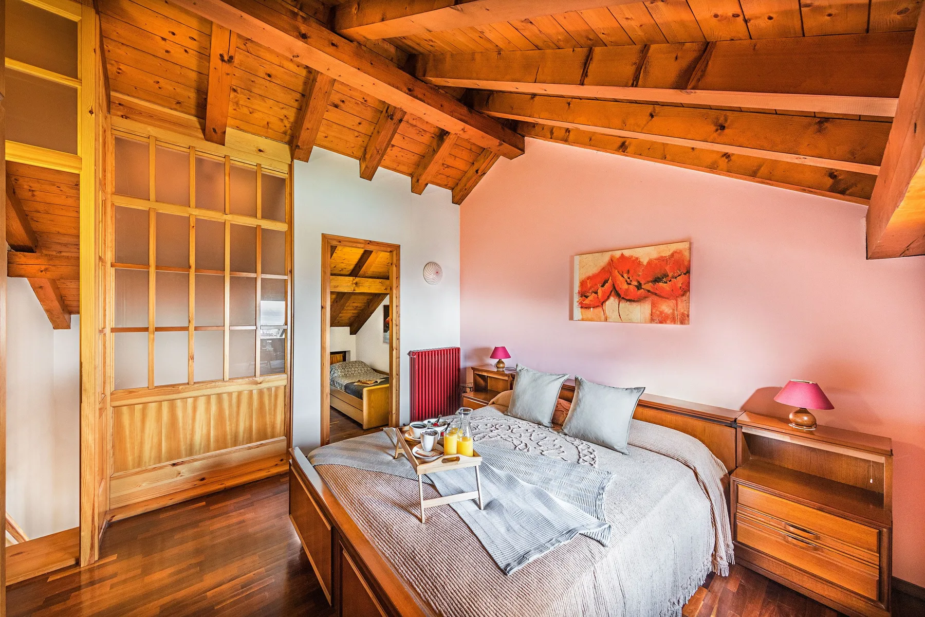A bedroom with a bed beneath a sloped wooden ceiling and exposed beams.