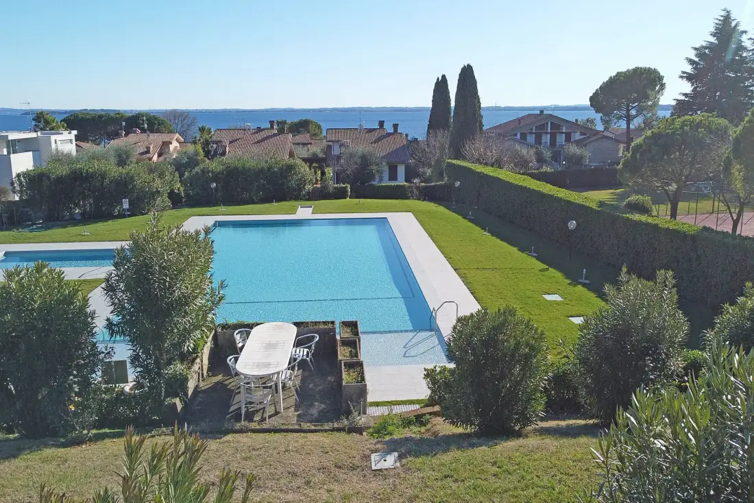 A swimming pool beside a grassy lawn, with houses and the sea in the distance.