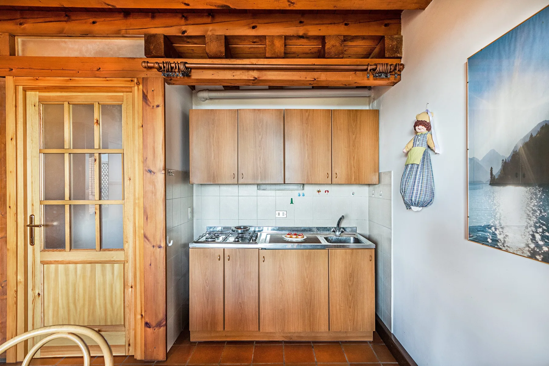 A compact kitchen with wooden cabinets sits beside a glass-paneled wooden door.