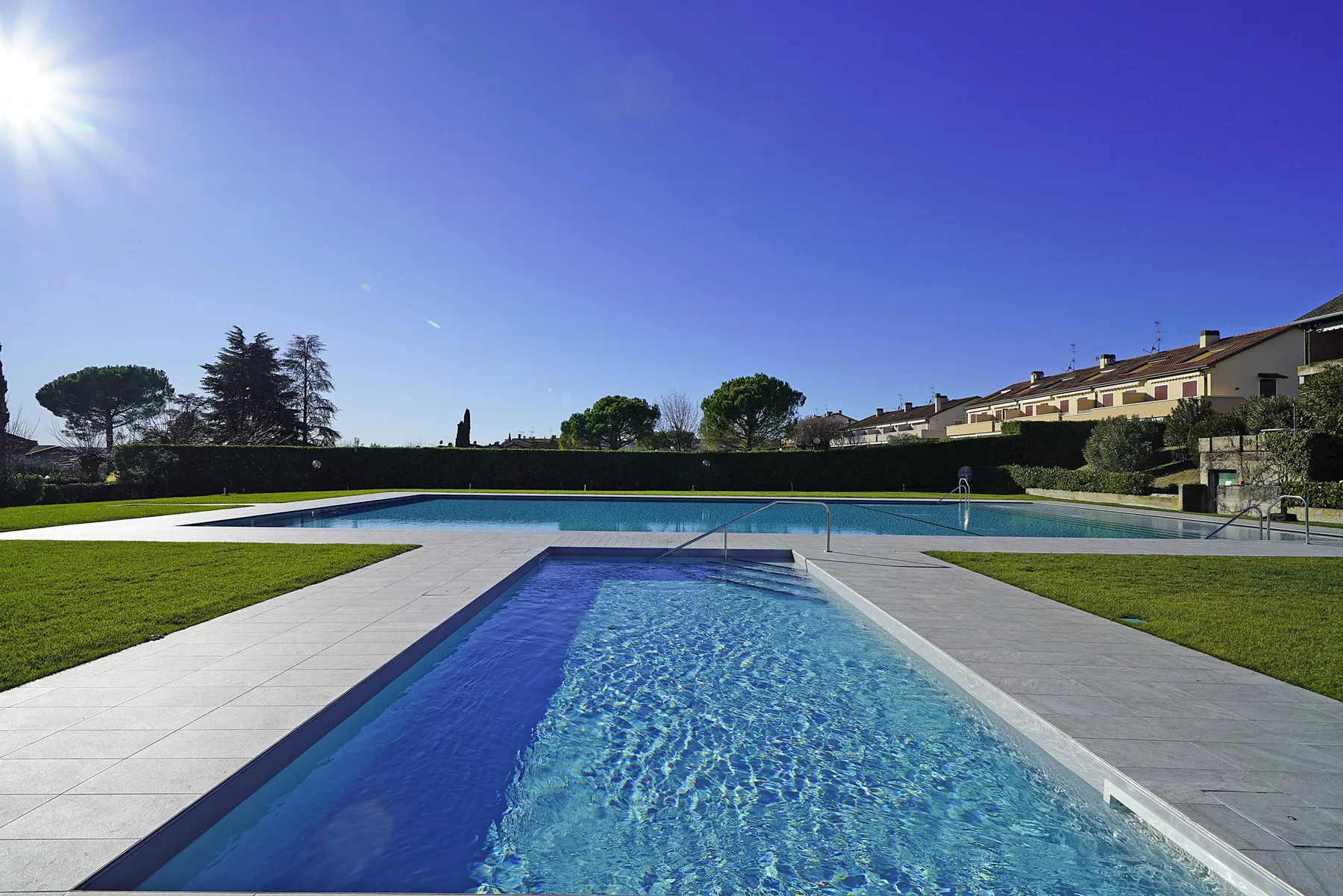 A swimming pool and smaller foreground pool sit beside a broad paved deck.