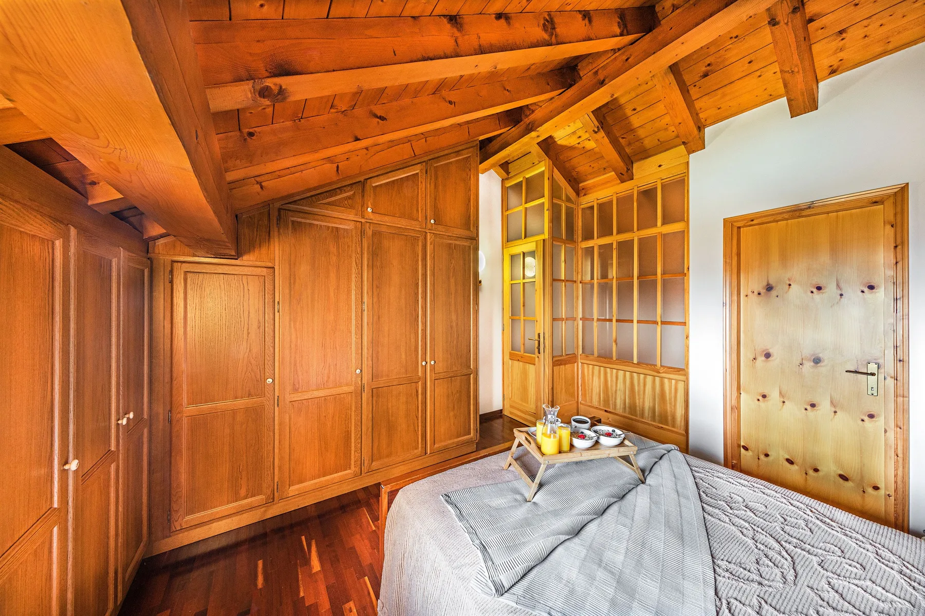 A bedroom with a bed beneath a sloped wooden ceiling and built-in cabinets.