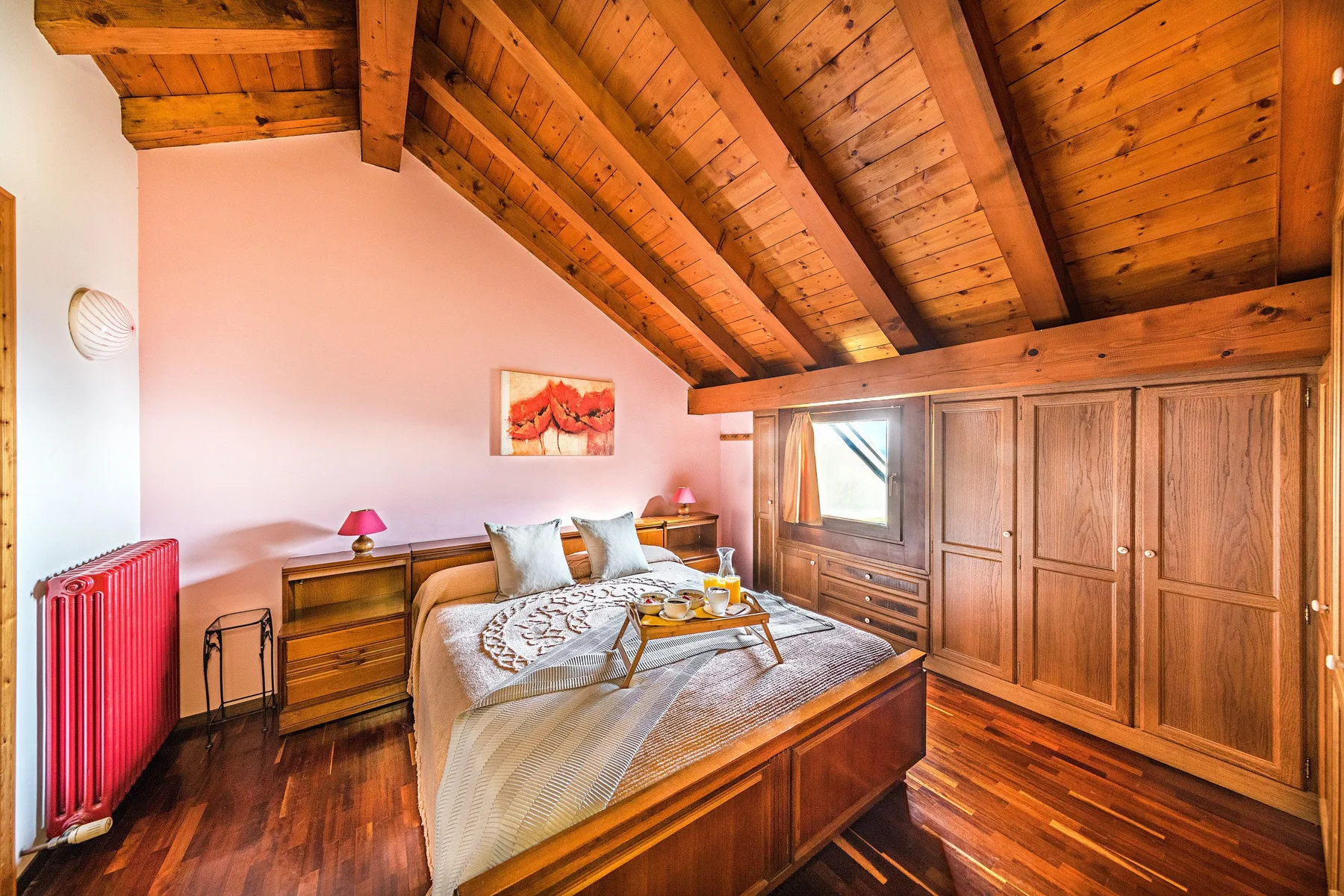 A bedroom with a bed beneath a sloped wooden ceiling and built-in wardrobes.