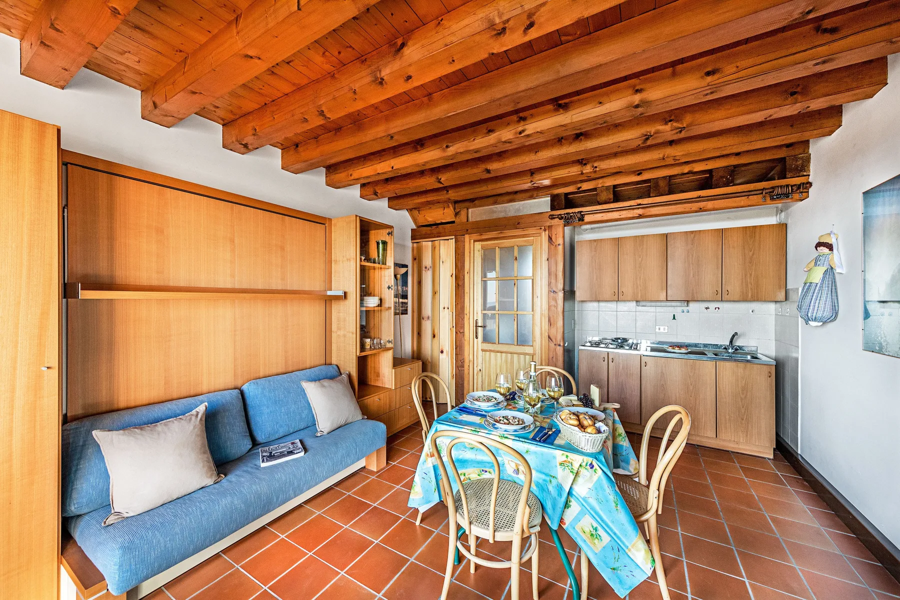 A rustic kitchen and dining area with a blue bench and a colorful tablecloth.
