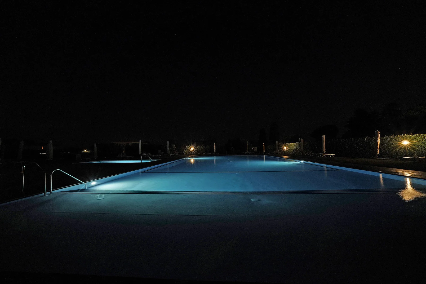 A swimming pool glows blue at night, with lights along the far edge.