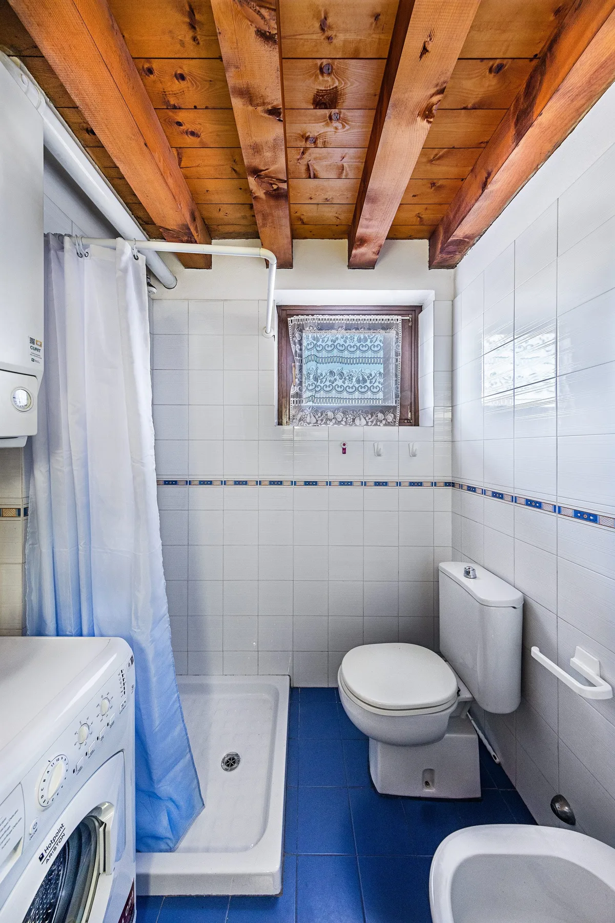 A tiled bathroom with a shower, toilet, and exposed wooden ceiling beams.