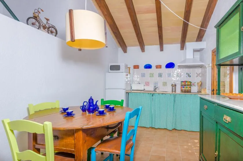 A dining area with a wooden table and colorful chairs beside a tiled kitchen.