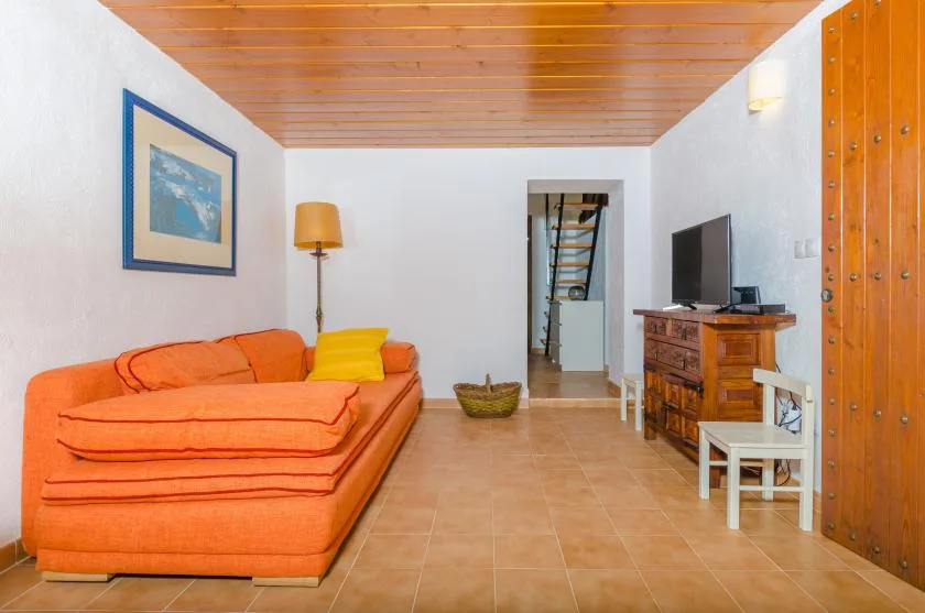 A living room with orange seating, a television, and a wooden ceiling.