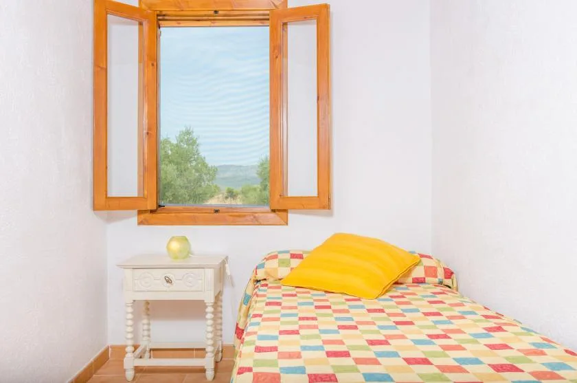 A bedroom with a colorful patchwork bedspread and an open window.