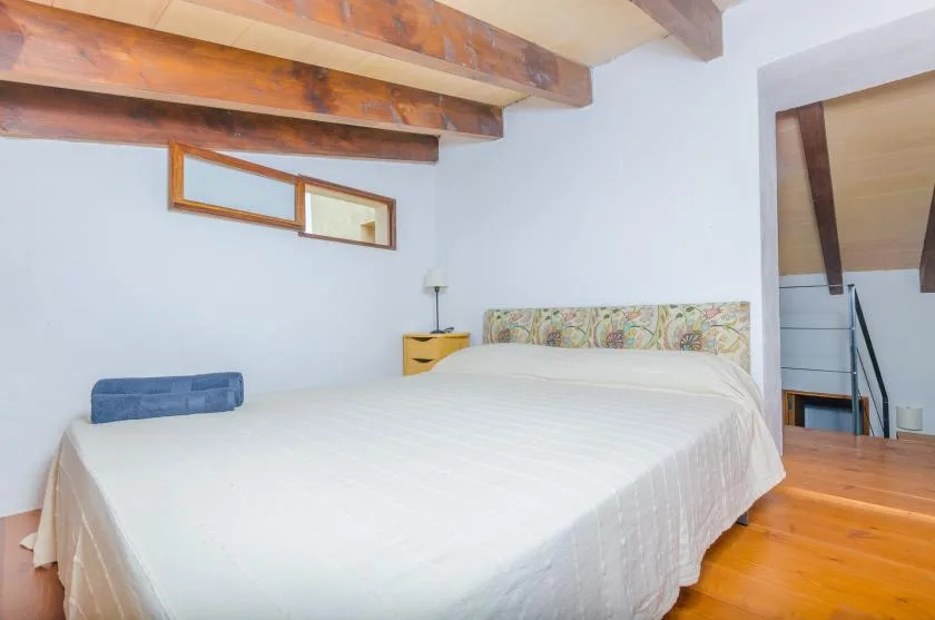 A bedroom with a large bed beneath exposed wooden ceiling beams.