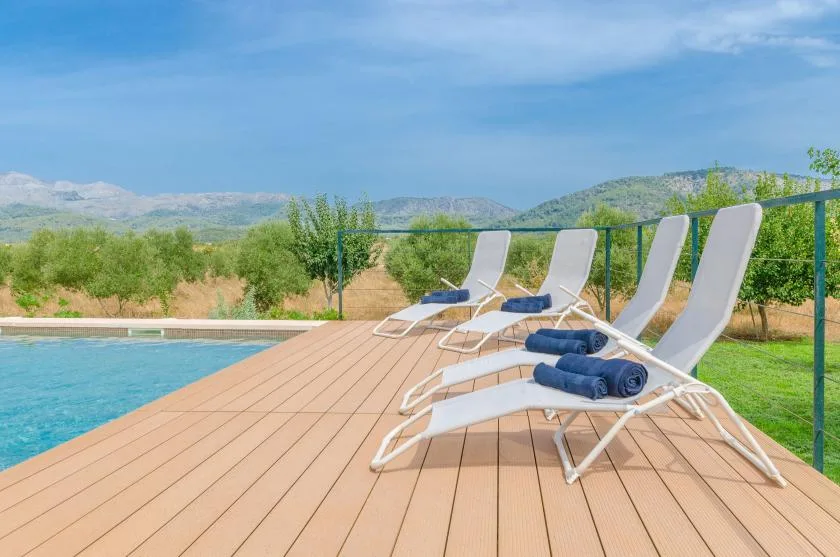 A poolside wooden deck has several lounge chairs with folded blue towels.