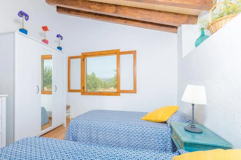 A bedroom with a blue patterned bed, a yellow pillow, and a wooden-framed window.
