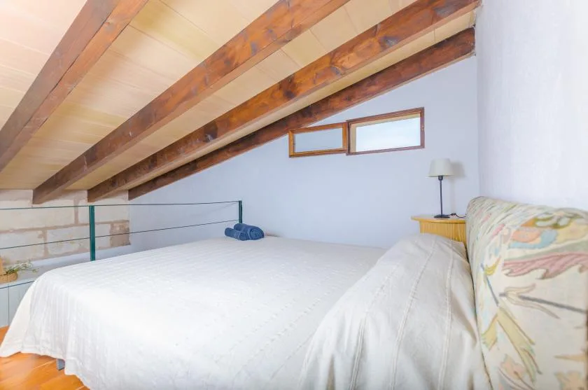A bedroom with a bed beneath a sloped ceiling with exposed wooden beams.
