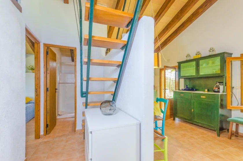 A kitchen with green cabinetry and a wooden staircase leading above.
