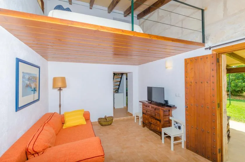 A living room with orange seating, a television, and a wooden mezzanine above.