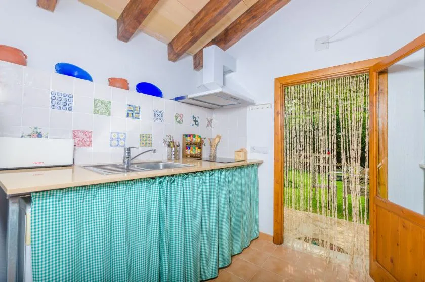 A small kitchen with a tiled backsplash, sink, and green checked curtains.