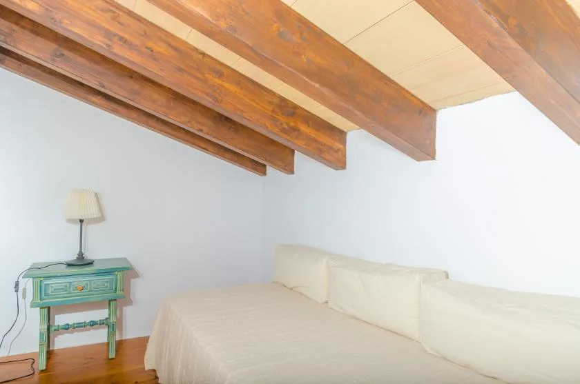 A bedroom with a bed beneath exposed wooden ceiling beams.