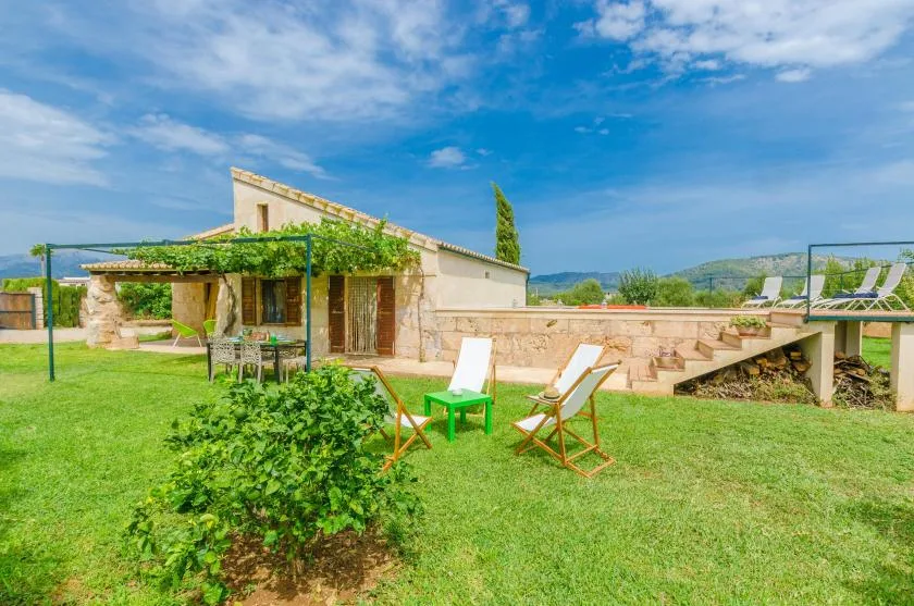 A stone house opens onto a green lawn with outdoor seating and a shaded patio.