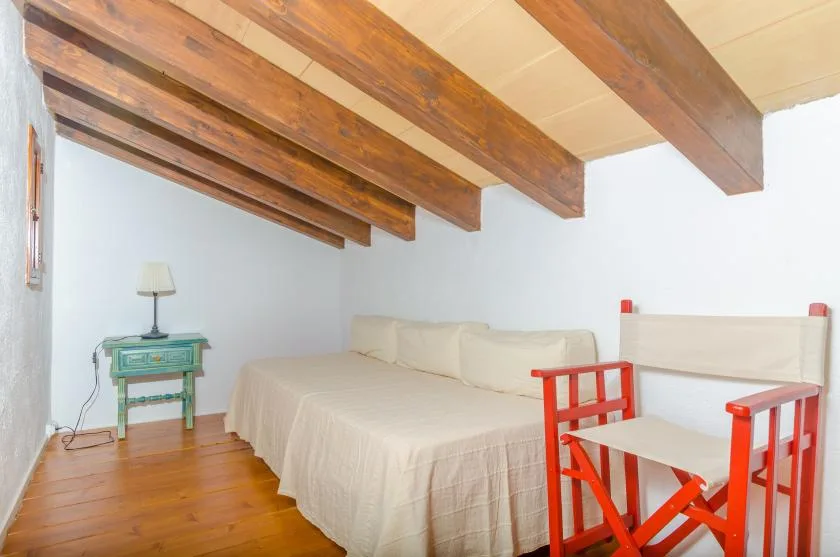 A bedroom with a bed, exposed wooden ceiling beams, and red seating.
