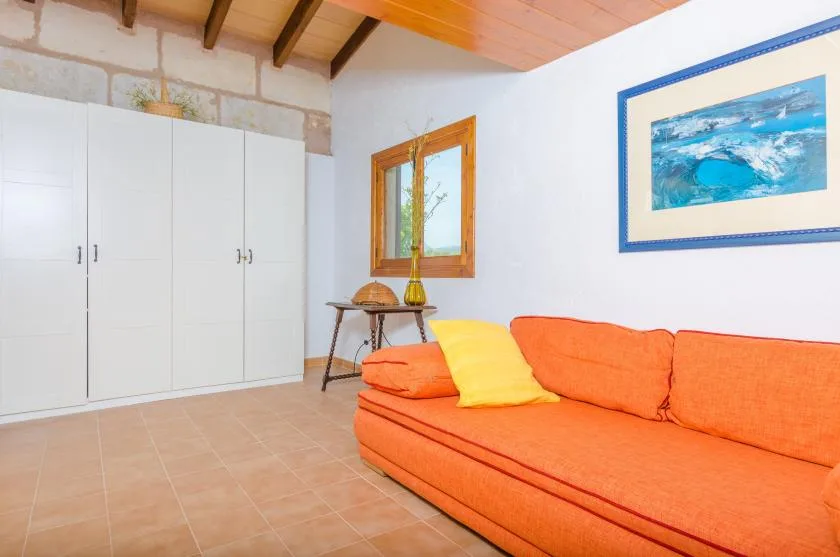 A living room with orange seating, white cabinets, and a framed blue picture.