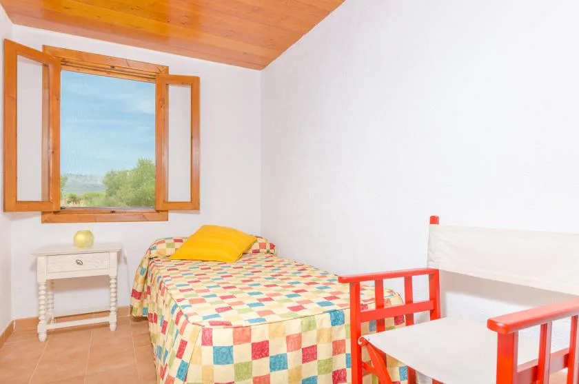 A bedroom with a colorful bed beside an open window.