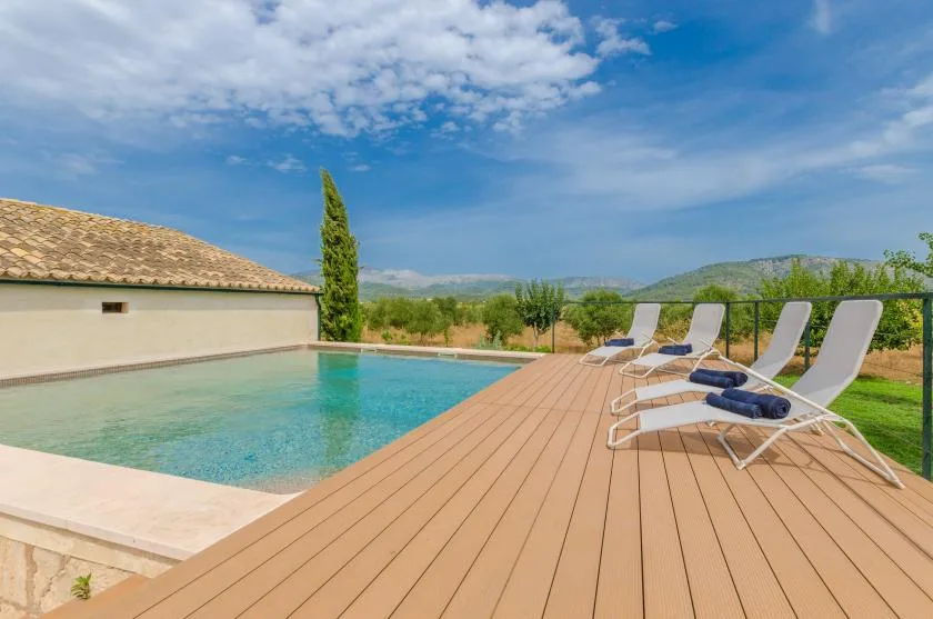 A swimming pool beside a wooden deck with lounge chairs under a blue sky.