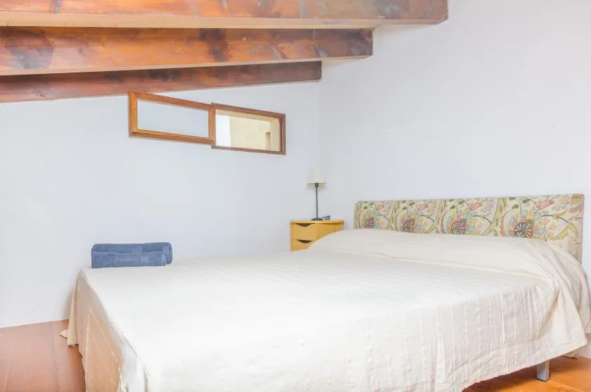A bedroom with a bed, patterned headboard, and exposed wooden beams.
