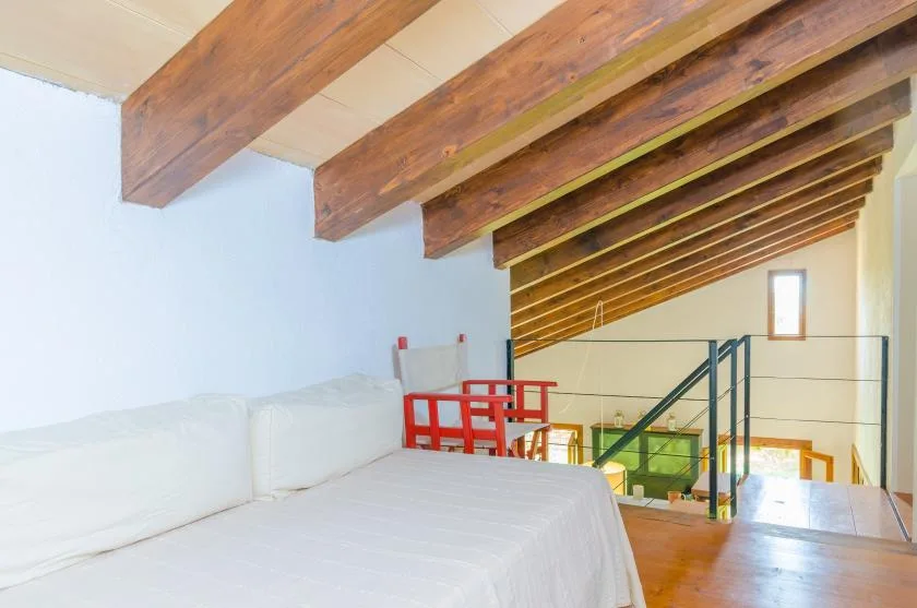 A loft bedroom has a bed beneath exposed wooden ceiling beams, overlooking a railing.