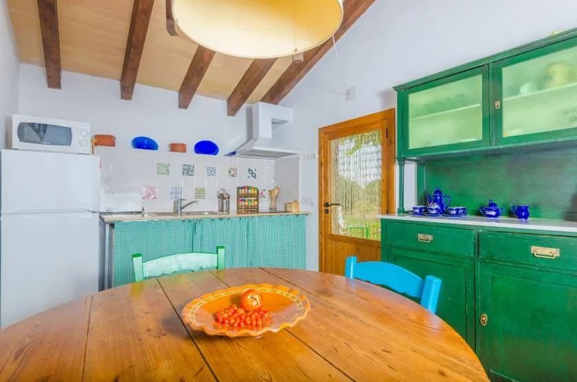 A kitchen with green cabinets, a refrigerator, and a wooden dining table.