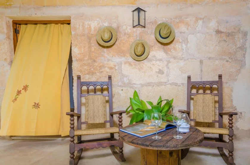 A rustic sitting area with two wooden chairs and a round table beside a curtained doorway.