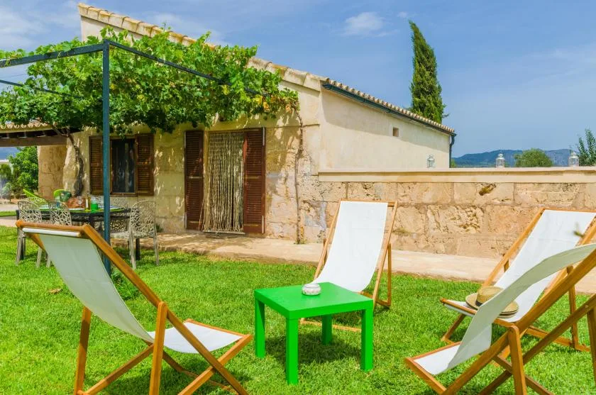 A grassy outdoor patio with reclining seats and a small green table beside a stone house.