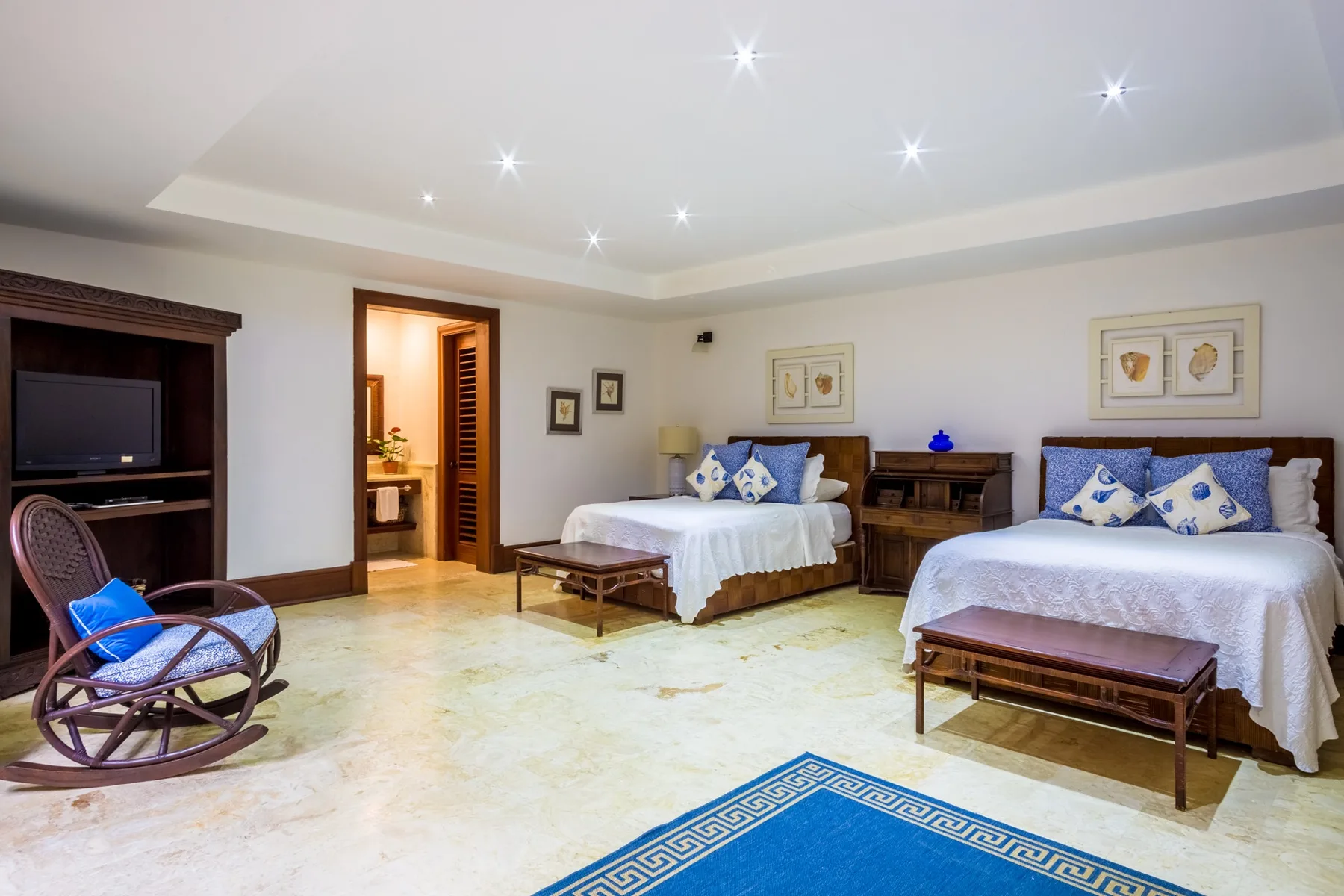 A bright bedroom with two beds, wooden furnishings, and recessed ceiling lights.