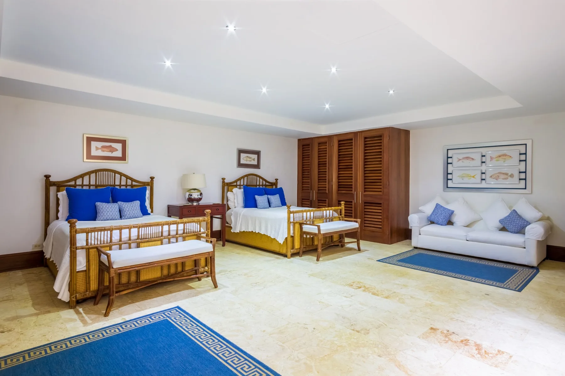 A bright bedroom with two beds, a seating area, and wooden wardrobes.