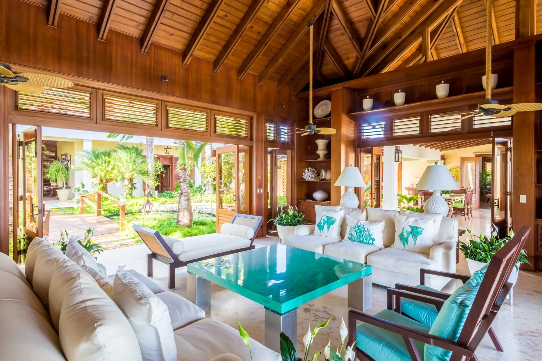 A spacious living room with pale seating and a glass coffee table opens onto a garden.