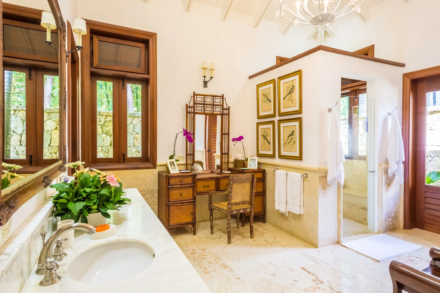 A bright bathroom with a marble vanity, wooden windows, and a bathing area.