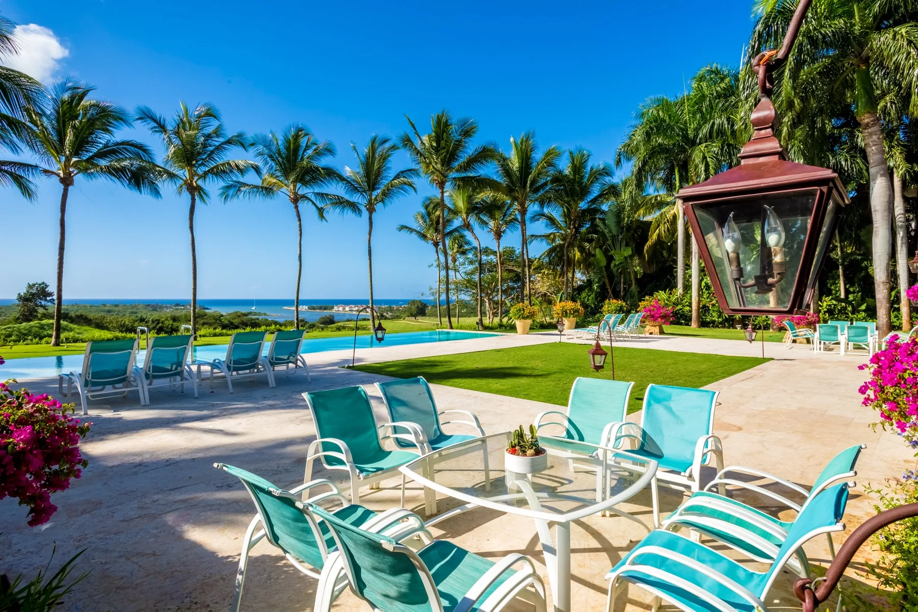 Outdoor seating and a swimming pool overlook the ocean beneath palm trees.