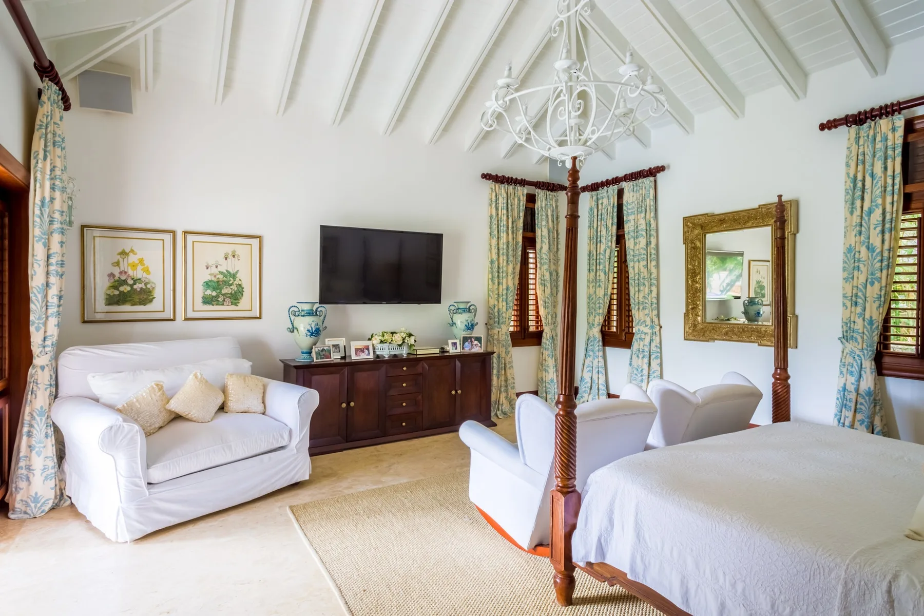 A bright bedroom with a bed, seating, and curtained windows.