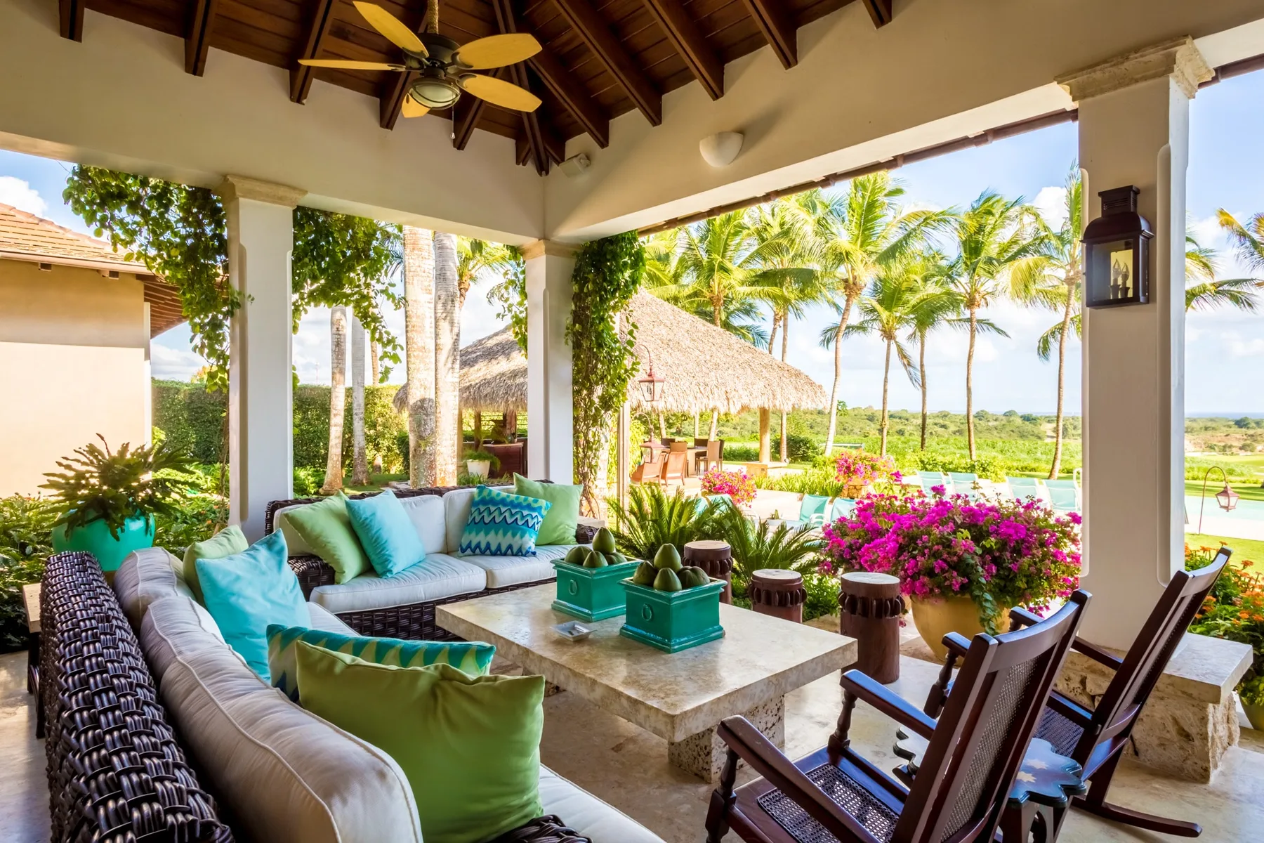 An open-air patio with cushioned seating and a view of palm trees and gardens.
