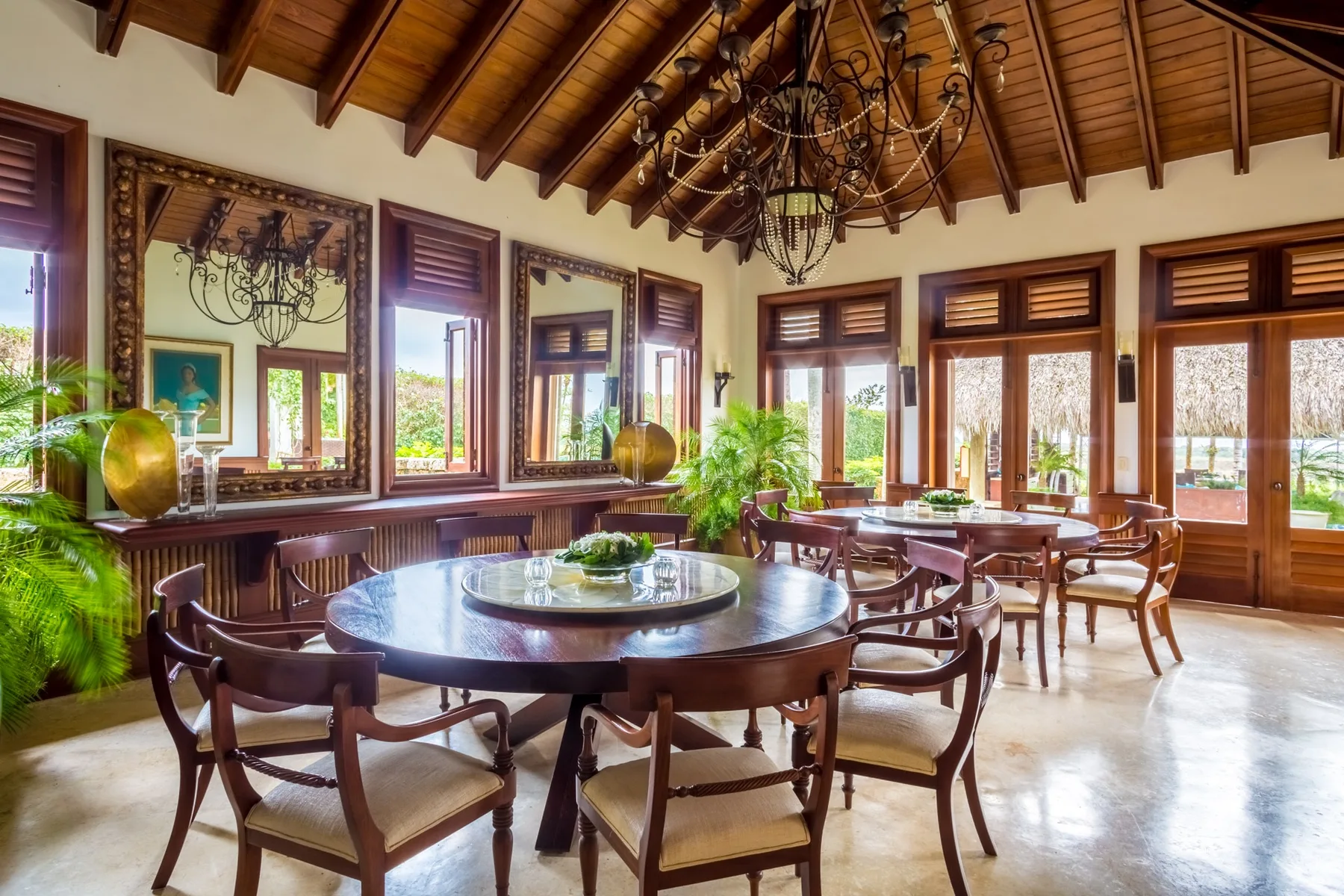 A bright dining room with a large round table beneath a wooden beamed ceiling.