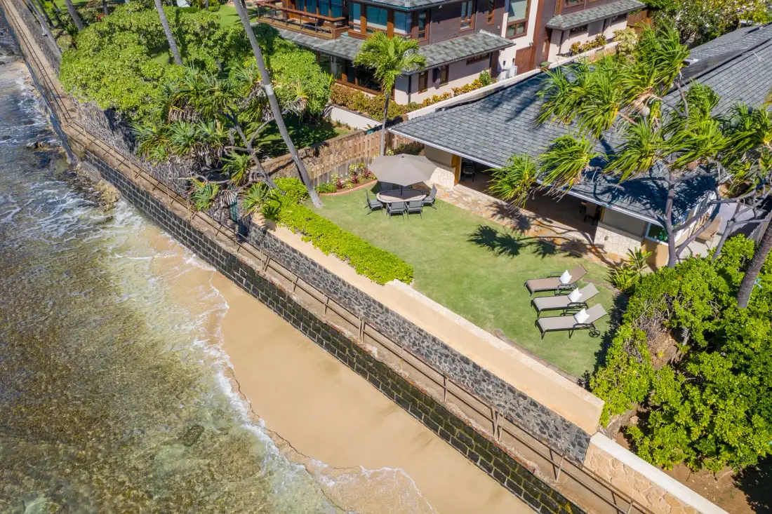 An aerial view shows a beachfront lawn with outdoor seating beside the shoreline.