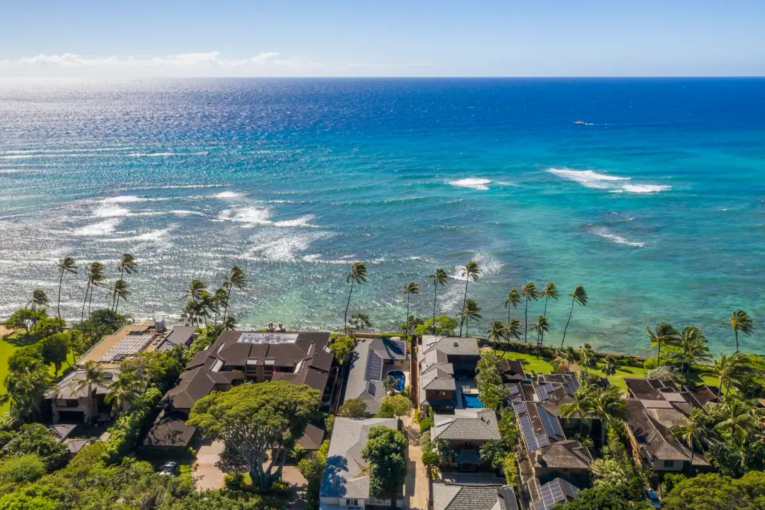 Aerial view of homes and palm trees along a turquoise coastline.