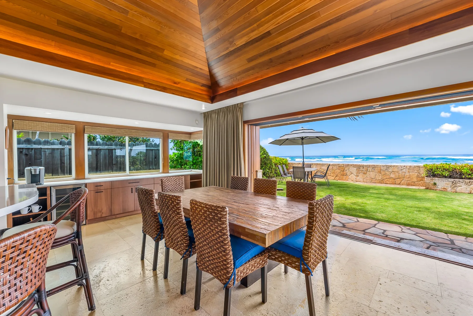 A dining area opens onto a lawn and ocean view through wide glass doors.