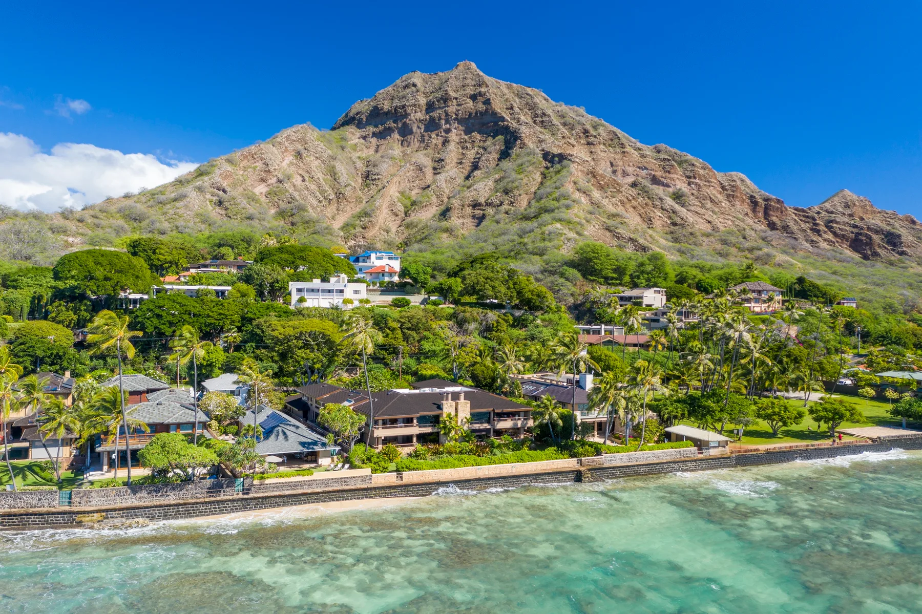 A coastal neighborhood sits beside clear water, with a rugged mountain rising behind it.