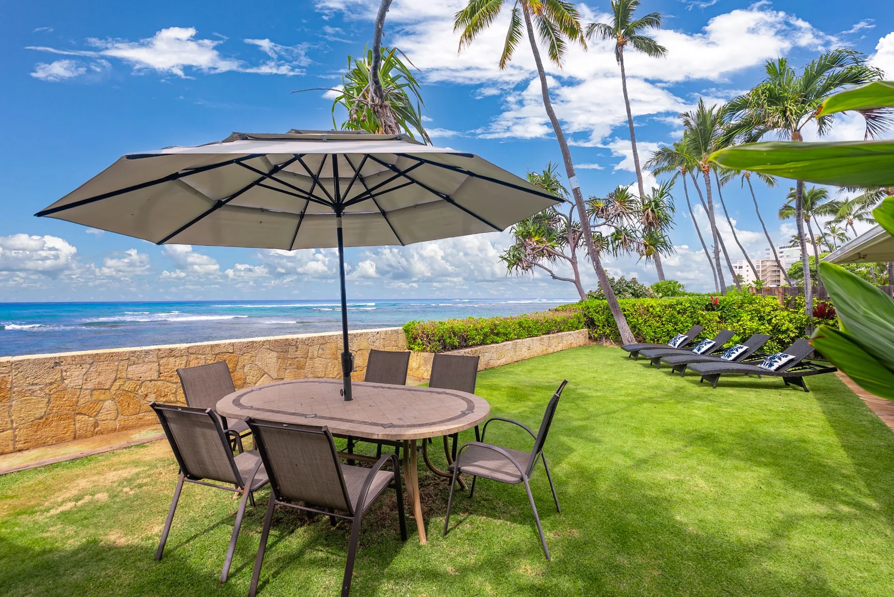 An outdoor patio with a table beneath an umbrella overlooks a lawn and ocean.