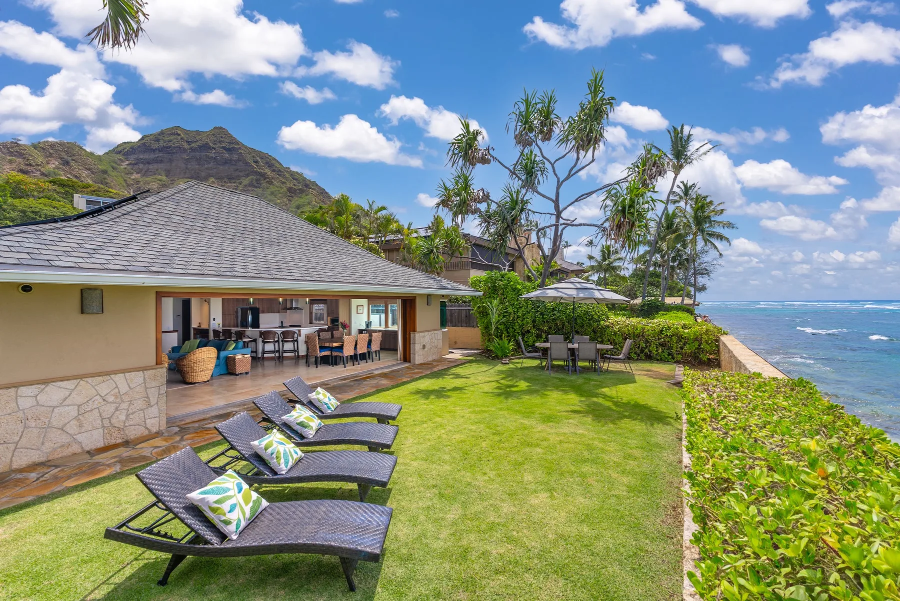 An outdoor lawn beside a house has lounge seating and views of the ocean.