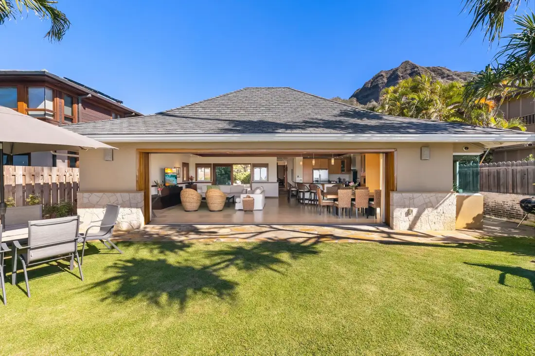 A single-story home opens onto a lawn, with a covered seating area.